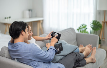 Asian couples embrace joy and excitement of pregnancy as they scan ultrasound images, revealing...