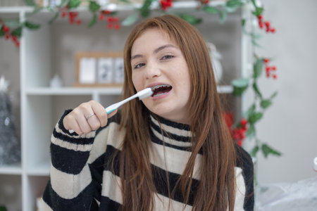 A mixed race teenage girl with dental braces smiles while holding a toothbrush in a festive decorated room.の写真素材