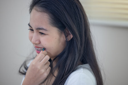 Cheerful Asian teenage girl with colorful dental braces laughing and enjoying a lighthearted moment...