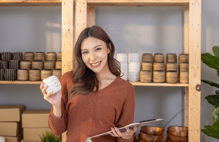 Confident and smiling business owners present handcrafted pottery in a warmly lit interior space.の写真素材