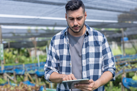 A veggie farm owner uses a tablet to inspect quality, monitoring growth as part of routine evaluations. Efficiently organized operations in greenhouse trays foster sustainable agricultural growth.の写真素材