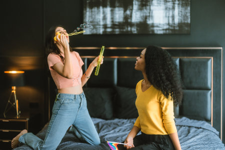 An LGBT couple enjoys a playful moment blowing and chasing bubbles on a bed, exuding happiness and carefree fun. The scene is filled with vibrant colors and a sense of inclusivity.の写真素材