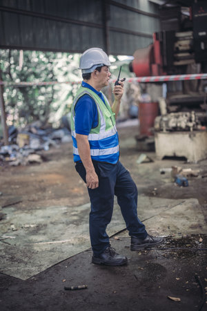 A safety inspector uses a walkie talkie to report an oil leak in an industrial setting. The image captures the critical moment of ensuring safety in a cluttered and potentially hazardous environment.の写真素材