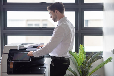 Professional businessman operates photocopy machine in modern office setting. The efficiency and routine of office tasks, highlighting the importance of document management in a corporate environmentの写真素材