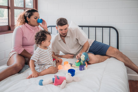 A joyful family moment captured in a cozy bedroom as parents engage with their young child in play with colorful toys, fostering love and bonding.の写真素材