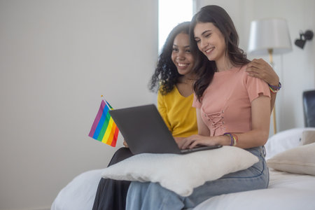 Tender moment of lesbian couple relaxing on bed, They enjoy browsing tablet together.  The Cozy bedroom setting adds to the intimate and warm atmosphereの写真素材