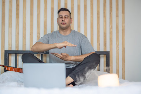 A man practicing meditation in a calm, dimly lit bedroom, with a laptop in front of him and a candle softly glowing nearby, creating a serene and focused atmosphere. Digital detox routineの写真素材