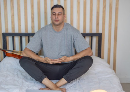 A man practicing meditation in a calm, dimly lit bedroom, with a laptop in front of him and a candle softly glowing nearby, creating a serene and focused atmosphere. Digital detox routineの写真素材