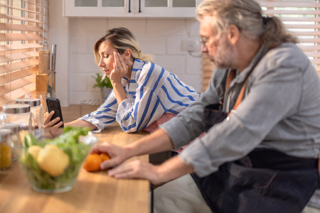 Woman playing smartphone , surrounded by warm morning light. The scene captures quiet pause during meal preparation, reflecting moment of relaxation in warm and inviting home kitchen.の写真素材