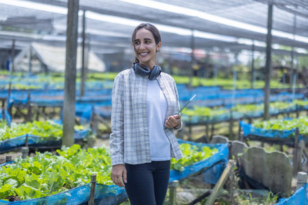 A farm owner wearing a plaid shirt and headphones stands confidently inside a greenhouse filled with...