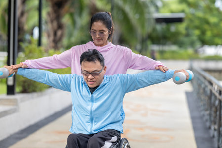 A man in a wheelchair exercising, supported by his partner during a resistance, strengthening and cardio workout routine. This image highlights the themes of fitness, motivation, and perseverance.の写真素材