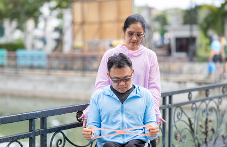 A man in a wheelchair exercising, supported by his partner during a resistance, strengthening and cardio workout routine. This image highlights the themes of fitness, motivation, and perseverance.の写真素材