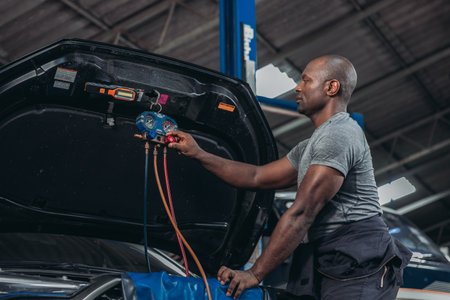 A skilled automotive technician uses manifold gauges to diagnose and service the air conditioning system of a vehicle in the garage workshop, ensuring optimal performance and efficiency.の写真素材