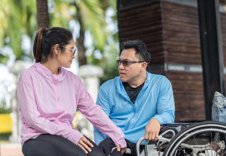 A couple shares an intimate and empathetic conversation while sitting outdoors. The man, in a wheelchair, engages attentively as they connect in a moment of mutual understanding and support.の写真素材