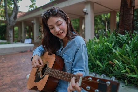 A young woman plays acoustic guitar in public space, immersed in music. Serene outdoor environment...