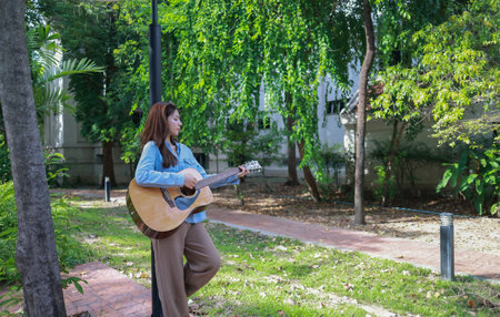 A young woman plays acoustic guitar in public space, immersed in music. Serene outdoor environment...