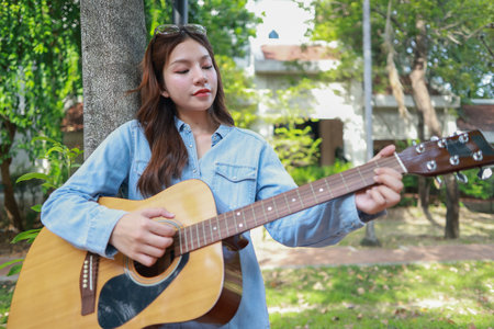 A young woman plays acoustic guitar in public space, immersed in music. Serene outdoor environment...