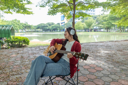 A young woman plays acoustic guitar in public space, immersed in music. Serene outdoor environment...