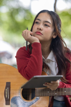 A young woman plays acoustic guitar in public space, immersed in music. Serene outdoor environment adds to calm and artistic vibe, creating a perfect backdrop for creative energy and performance.の写真素材