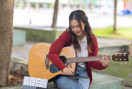 A young woman plays acoustic guitar in public space, immersed in music. Serene outdoor environment...