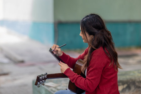 A young woman plays acoustic guitar in public space, immersed in music. Serene outdoor environment adds to calm and artistic vibe, creating a perfect backdrop for creative energy and performance.の写真素材