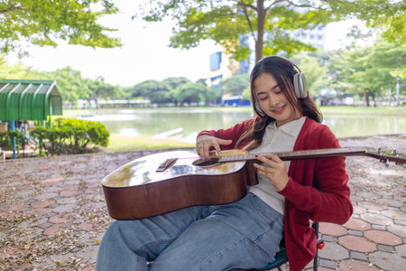 A young woman plays acoustic guitar in public space, immersed in music. Serene outdoor environment adds to calm and artistic vibe, creating a perfect backdrop for creative energy and performance.の写真素材