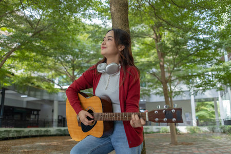 A young woman plays acoustic guitar in public space, immersed in music. Serene outdoor environment...