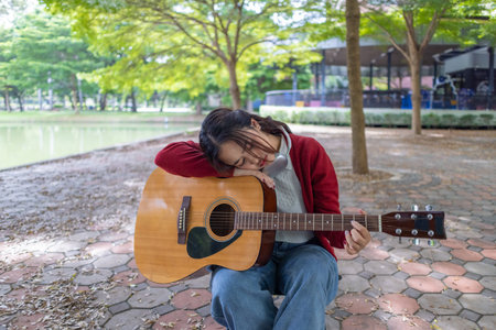 A young woman plays acoustic guitar in public space, immersed in music. Serene outdoor environment adds to calm and artistic vibe, creating a perfect backdrop for creative energy and performance.の写真素材