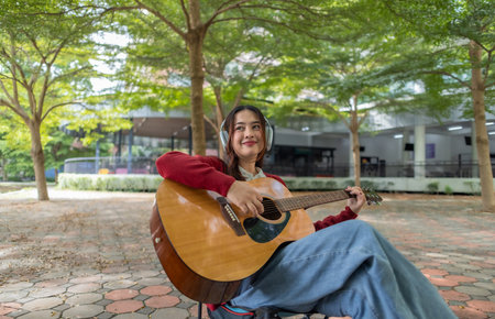 A young woman plays acoustic guitar in public space, immersed in music. Serene outdoor environment...