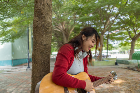 A young woman plays acoustic guitar in public space, immersed in music. Serene outdoor environment...
