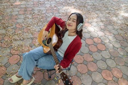 A young woman plays acoustic guitar in public space, immersed in music. Serene outdoor environment...
