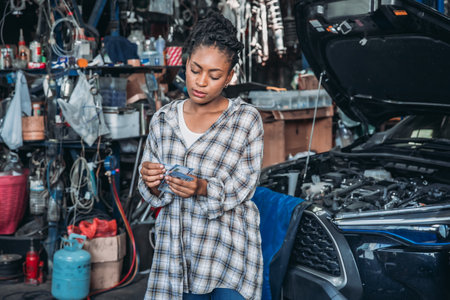 A young woman stands in a bustling automotive garage, inspecting a repair receipt. Tools and car parts surround her as she focuses on the details, demonstrating her engagement in automotive work.の写真素材