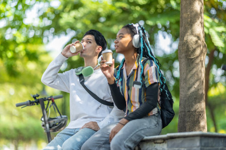 Diverse pair of young adults enjoying a break in urban park with electric scooter and bicycle nearby. Sustainable commuting and casual atmosphere highlights modern lifestyle, eco friendly travelの写真素材