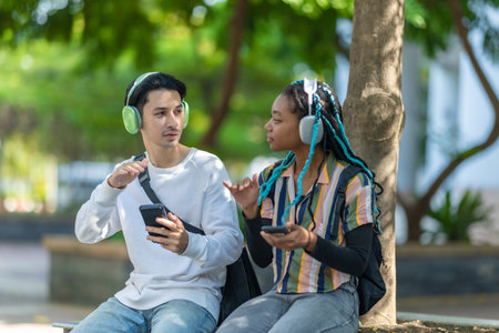 Diverse pair of young adults enjoying a break in urban park with electric scooter and bicycle nearby. Sustainable commuting and casual atmosphere highlights modern lifestyle, eco friendly travelの写真素材