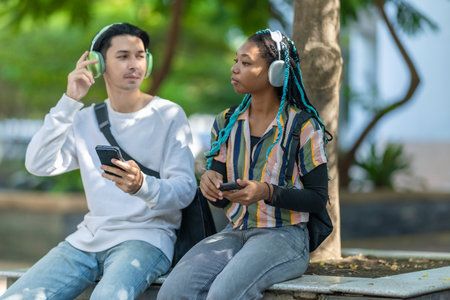 Diverse pair of young adults enjoying a break in urban park with electric scooter and bicycle nearby. Sustainable commuting and casual atmosphere highlights modern lifestyle, eco friendly travelの写真素材
