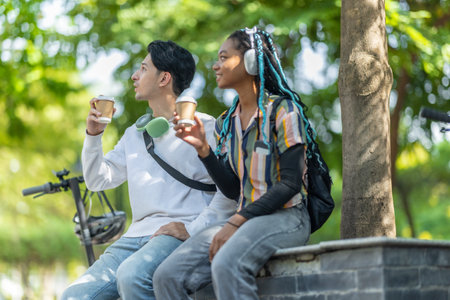 Diverse pair of young adults enjoying a break in urban park with electric scooter and bicycle nearby. Sustainable commuting and casual atmosphere highlights modern lifestyle, eco friendly travelの写真素材