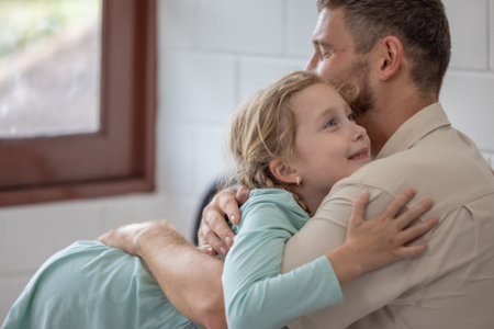A man and his daughter are embracing on a bed covered with white sheets. The room is bright, and they both share smiles, creating a warm family atmosphere on a peaceful morning.の写真素材