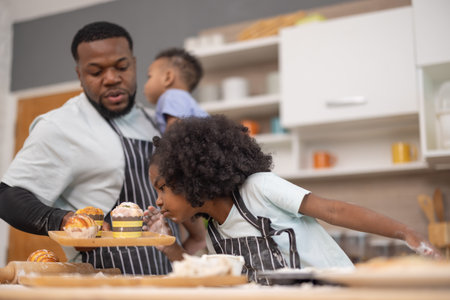 A father and his two children prepare treats in a cozy kitchen. They are mixing ingredients and having fun while covered in flour, illustrating joyful bonding moments.の写真素材