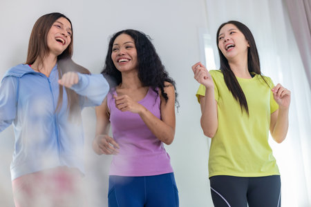 A lively group of three multicultural friends enjoying a casual dance session indoors. They appear cheerful and relaxed, wearing casual athletic clothing, emphasizing friendship, fun, and movementの写真素材