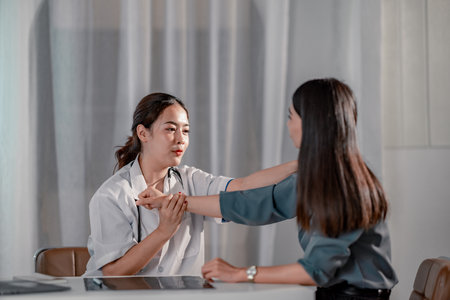 Asian female orthopedic doctor conducting physical examination of patient's arm in clinical setting. The scene captures a professional healthcare interaction focused on diagnosis and patient care.の写真素材