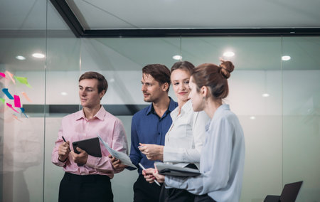 Businesspeople in a modern office, use sticky notes on glass wall for brainstorming and strategic planning. Idea organization, and project management in a corporate environment.の写真素材