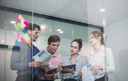 Businesspeople in a modern office, use sticky notes on glass wall for brainstorming and strategic planning. Idea organization, and project management in a corporate environment.の写真素材