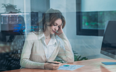 Fatigued and stressed businesswoman experiencing office syndrome while working late at desk. Long hours and excessive screen time lead to physical and mental exhaustion from extended working hours.の写真素材