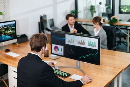 Financial analyst working on multiple monitors displaying stock market charts, financial data, and...