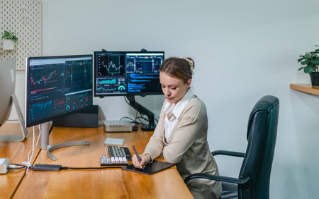 Financial analyst working on multiple monitors displaying stock market charts, financial data, and...