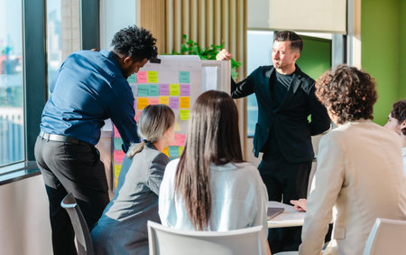 A diverse startup team engages in a discussion about work progress using an agile task board. The...