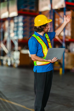 A warehouse supervisor wearing a safety vest and helmet using a digital device to manage operations...