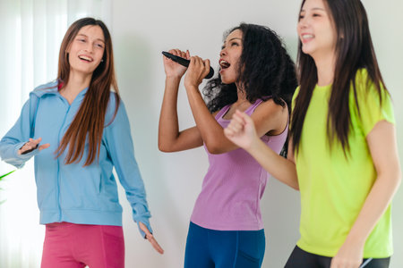 A group of three young multicultural friends singing and enjoying a karaoke session indoors. They are laughing and having fun, creating a joyful and energetic atmosphere.の写真素材