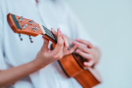 An Asian woman with curly, two-tone hair plays ukulele in an outdoor setting, radiating happiness and musical energy. A relaxed and artistic vibe with a natural backgroundの写真素材