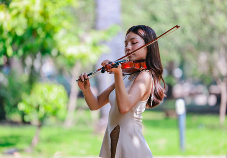 A young Asian woman gracefully practices the violin in a peaceful outdoor setting surrounded by lush greenery. Capturing a moment of musical concentration and tranquillity in nature.の写真素材